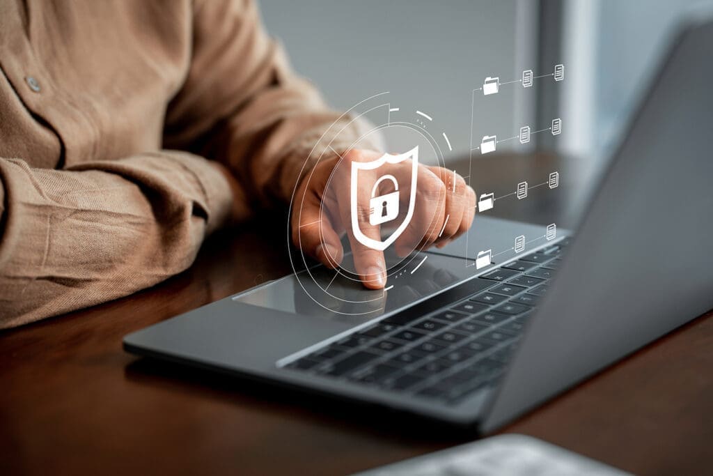 Person using a laptop with a digital cybersecurity shield icon overlay.