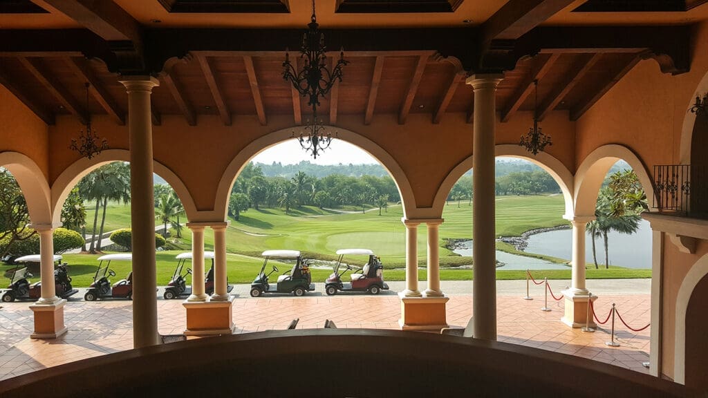 A view between arched architecture overlooking green grass and a row of golf carts.