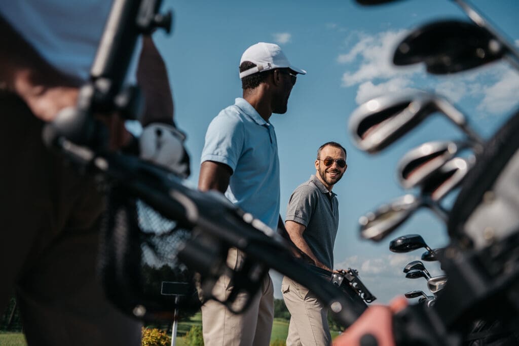 Two golfers smile at each other as they push their clubs.