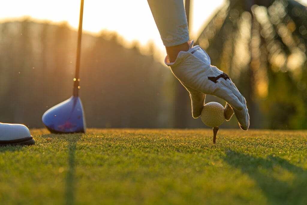 A person putting a ball on a tee for golfing.