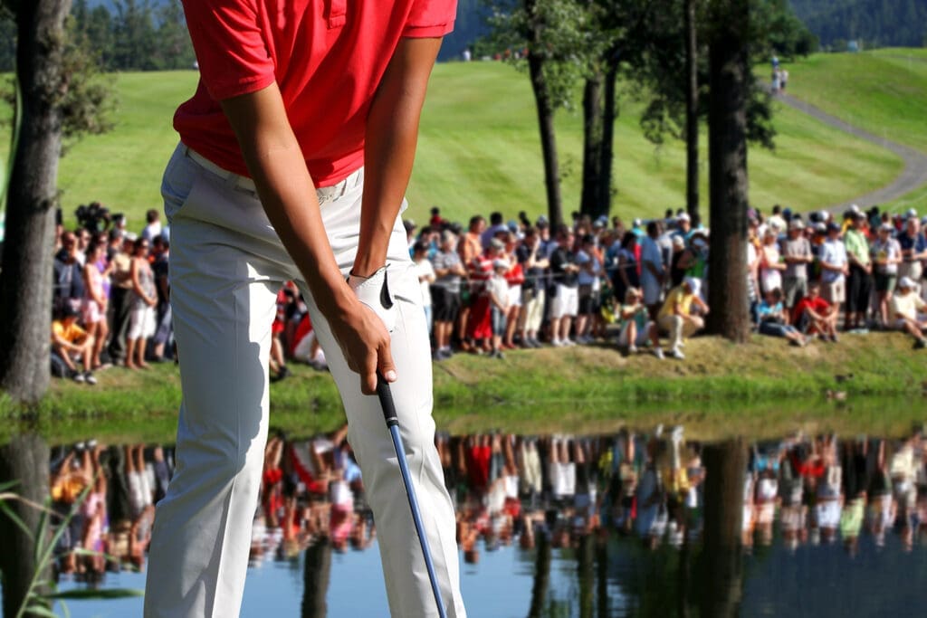 A group of spectators watching a person in a red shirt playing golf.